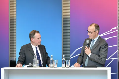 Fraktions-Enquete Frieden und Sicherheit in Europa. Friedrich Merz spricht auf dem Podium mit dem Historiker mit Historiker Niall Ferguson. Sie stehen an einem Tisch.