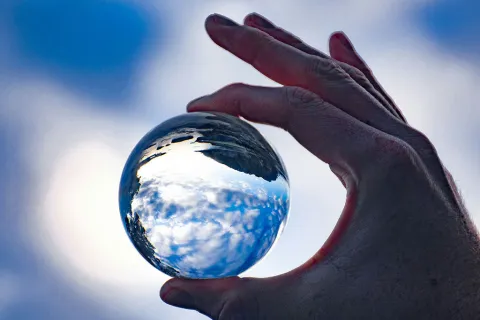 Eine Hand hält eine Glaskugel in der sich die Umwelt spiegelt 