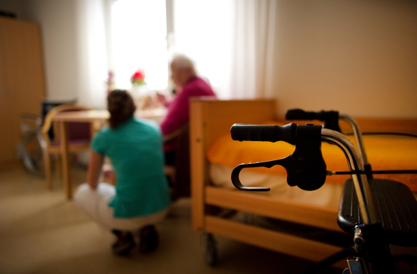 Pflegekraft kniet neben Seniorin im Pflegeheim
