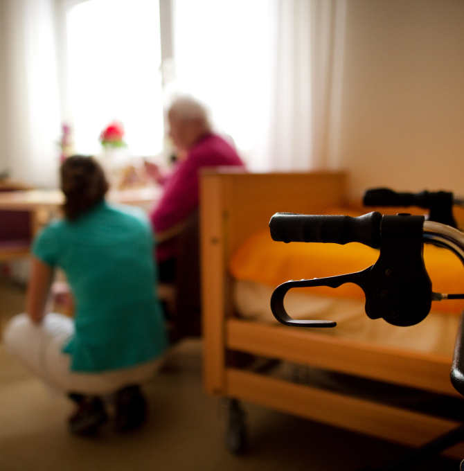 Pflegekraft kniet neben Seniorin im Pflegeheim