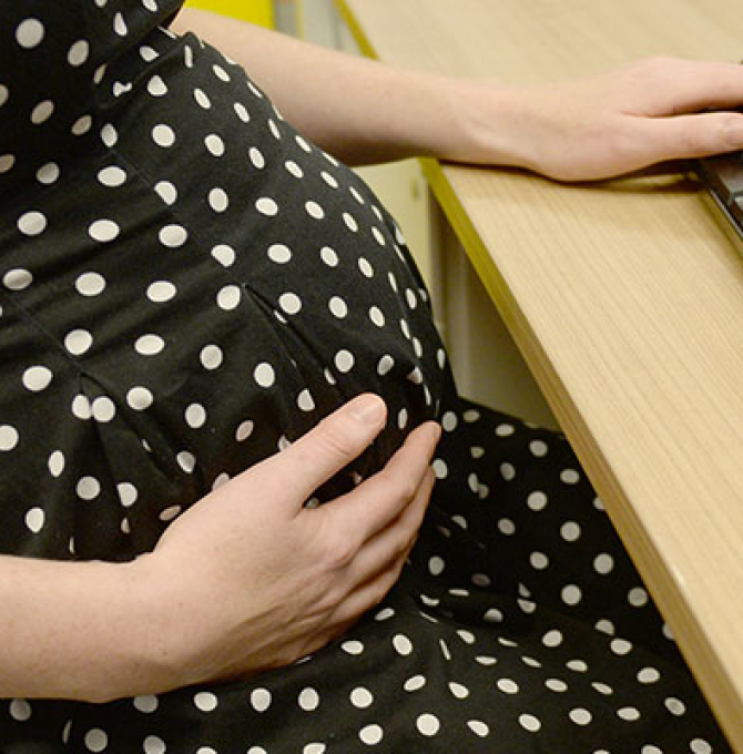 Eine Schwangere hält schützend die Hände vor den Bauch