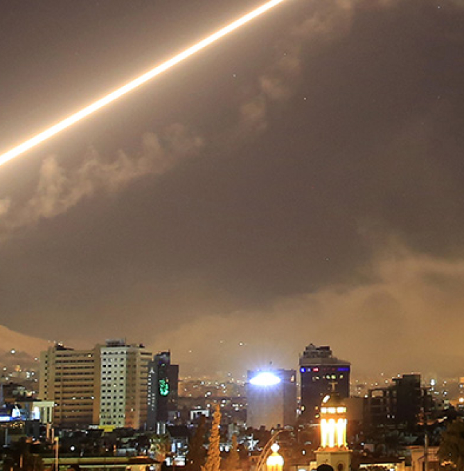 Das Bild zeigt oben den hellen Schweif einer Rakete vor dunklem Nachthimmel. Unten ist die Stadt Damaskus zu sehen.