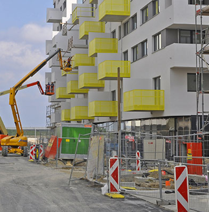 Das Bild zeigt eine Vielzahl noch im Bau befindlicher, weißer Häuser vor blauem Himmel. Im Vordergrund befindet sich eine Baustelle.