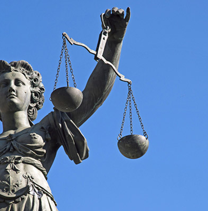 Das Bild zeigt eine Statue der Justizia, einen Arm nach vorne gestreckt hält sie eine Waage bestehend aus zwei Waagschalen. im Hintergrund: blauer Himmel. 