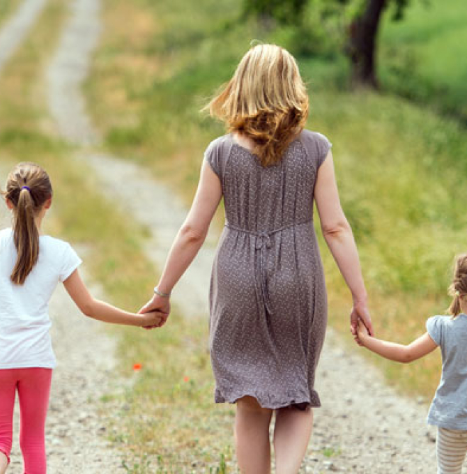 Eine Mutter und ihre beiden Töchter gehen einen Feldweg entlang