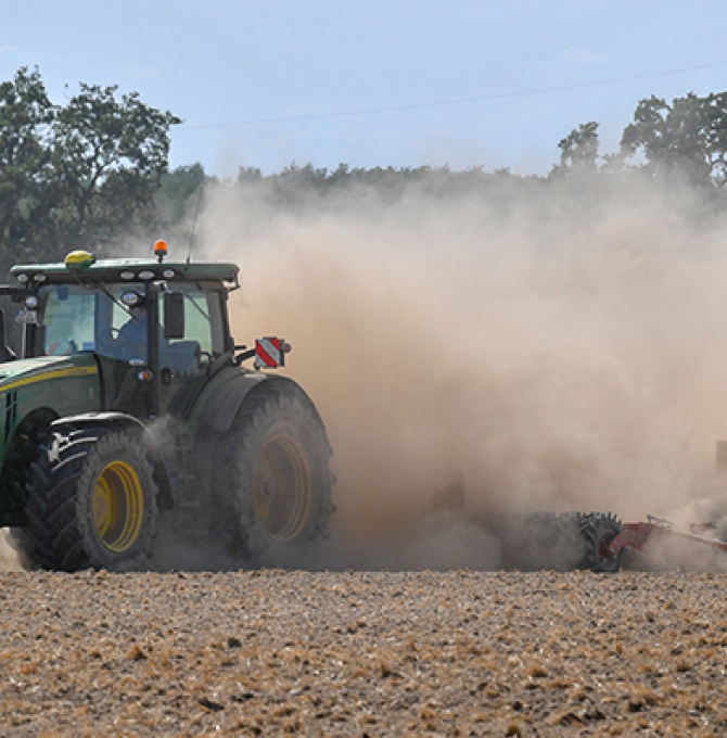 Traktor fährt über trockenes Feld, eine Staubwolke hinter sich herziehend