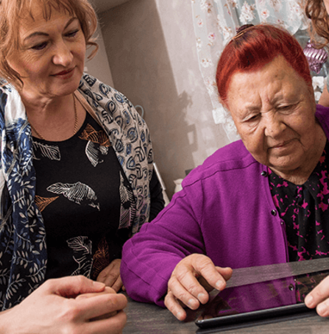 Familienmitglieder helfen einer älteren Frau, die auf ein Tablet schaut